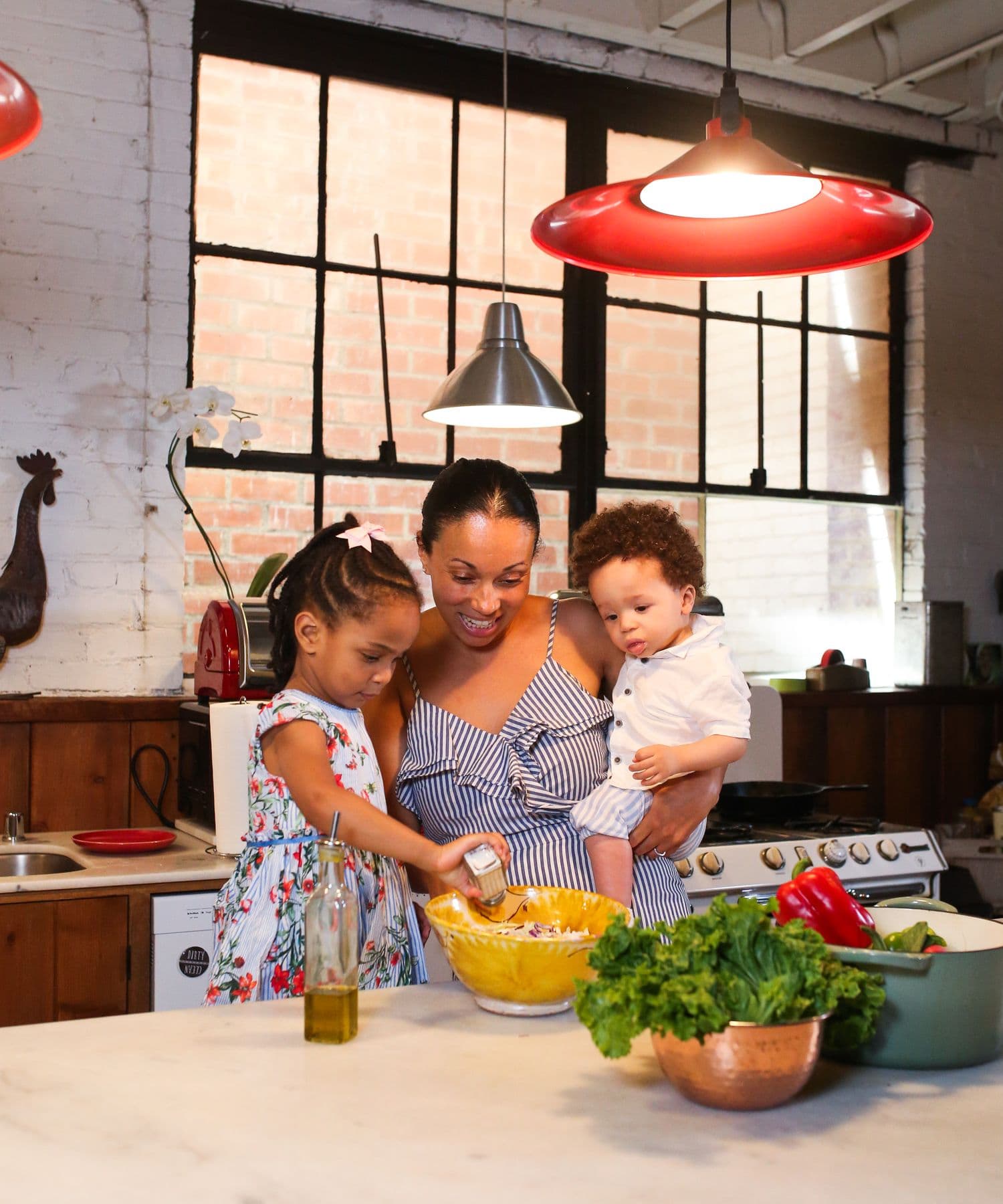 A mother holds her son while her daughter helps prepare food in their kitchen